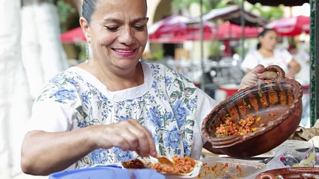 当地的墨西哥妇女准备街头食物在她的摊位在帕克圣露西亚，梅里达。视频下载