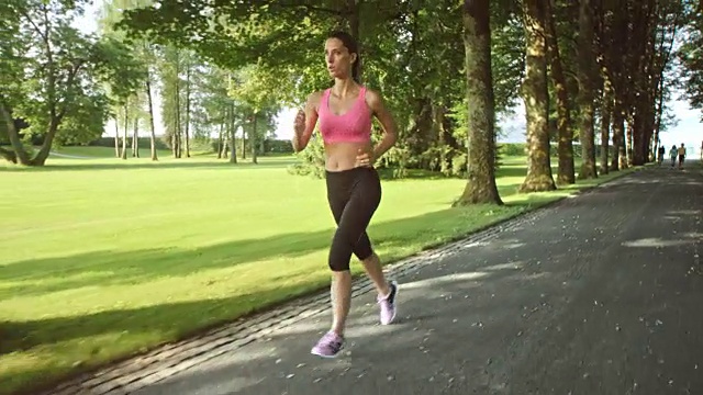 一个听着音乐在林荫小道上慢跑的女人视频素材
