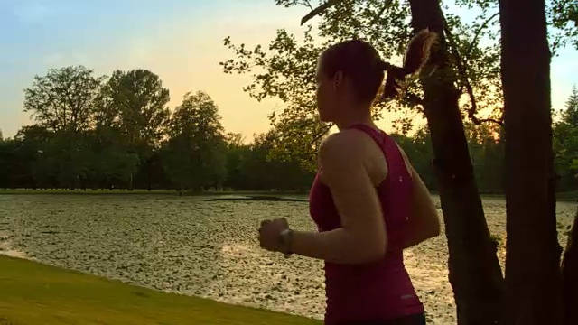 SLO MO TS女人在日落时沿着湖跑视频素材