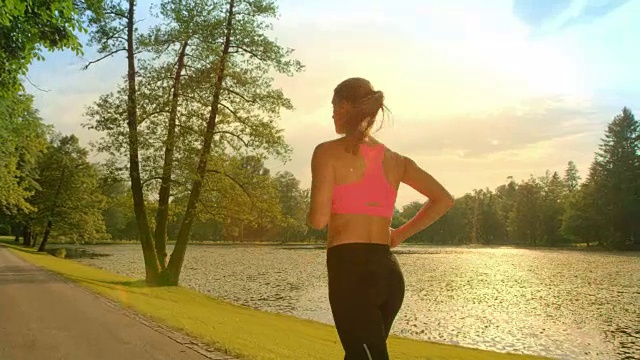 SLO MO黑发女子在阳光下沿着湖边奔跑视频素材
