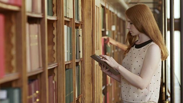 一名年轻女子在图书馆用平板电脑找一本书视频素材