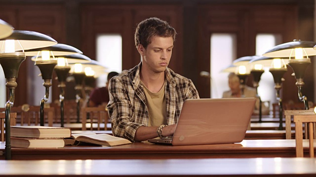 一个年轻人在图书馆里用笔记本电脑工作视频素材