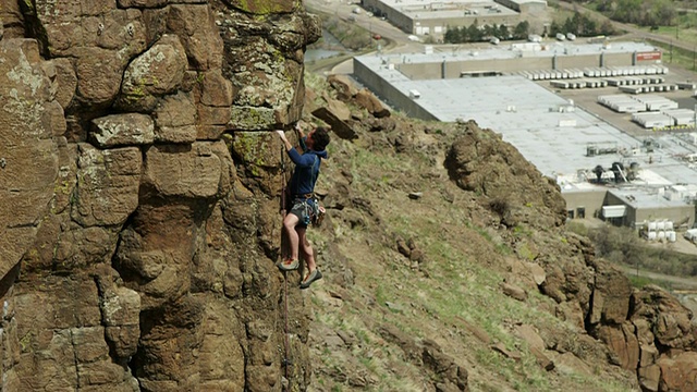 人爬上陡峭的岩石表面，下面有建筑物。视频素材