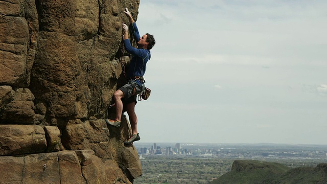一名男子爬上陡峭的岩石面，背景是丹佛市视频下载