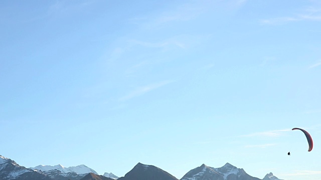 远方的人在蓝天上滑翔，在白雪皑皑的山峰上视频下载