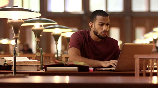 一个非裔美国学生在图书馆里用笔记本电脑学习视频下载