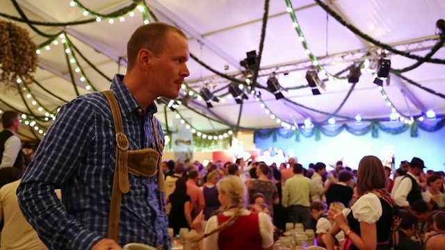 德国巴伐利亚州慕尼黑，传统啤酒节上，身着传统服饰的男子一边喝着啤酒瓶，一边跳舞视频素材