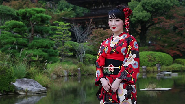 CU摄于日本山口县山口，一名日本女子穿着和服微笑地站在日本传统花园前视频素材