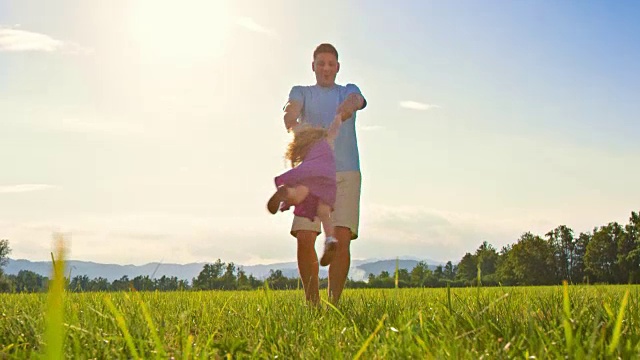 父亲带着女儿在阳光明媚的草地上旋转视频素材