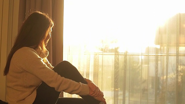 年轻女子坐在床上欣赏阳光。视频素材