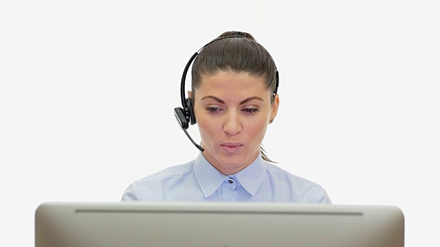 年轻女子在电脑前通过耳机说话。视频素材