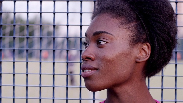 手持慢动作女子运动员站在栅栏前看镜头，微笑的背景是足球场视频素材