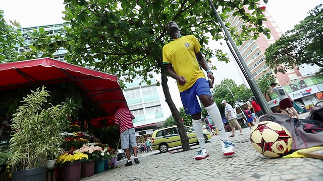 在巴西里约热内卢的一个街角，一个有色人种拿着巴西三叉戟玩自由式足球视频素材