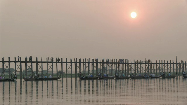 缅甸曼德勒省，曼德勒，人们过桥和几艘船在桥前的水里视频素材