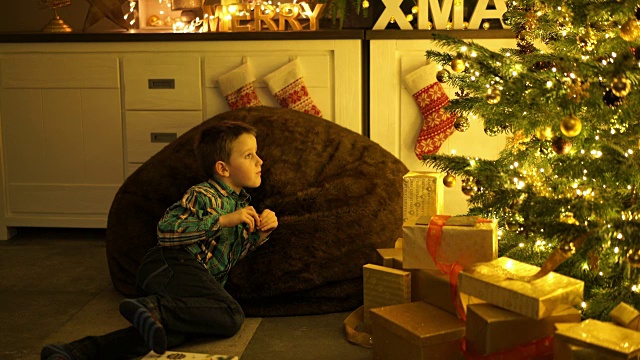 一个小男孩在客厅里看着点亮的圣诞树视频素材