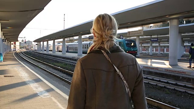 一名女子在站台上查看手机，等待火车视频下载