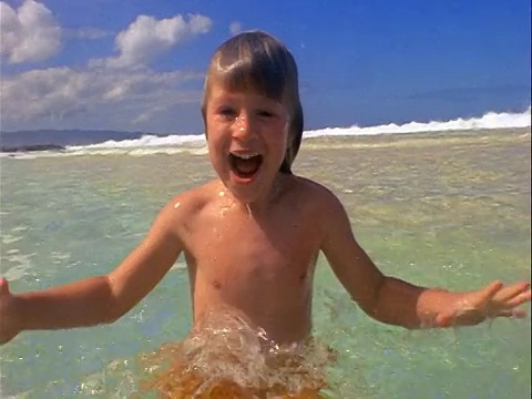 慢镜头水下+水上男孩游泳在海洋/表面的浅水+溅水视频下载