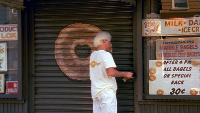 从百吉饼店的标牌倾斜到打开链条的白发男子+举起金属门/纽约视频下载