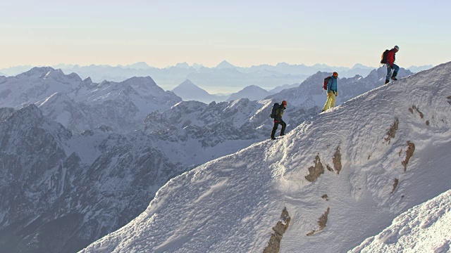 登山队员们在阳光下沿着雪山山脊前进视频素材