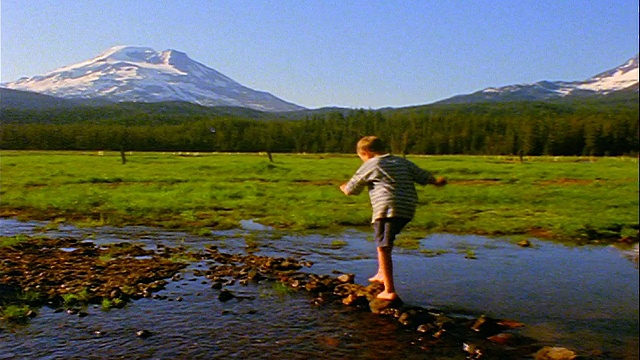 慢镜头男孩走在溪流/火花草地的岩石上，喀斯喀特山脉，俄勒冈州视频下载