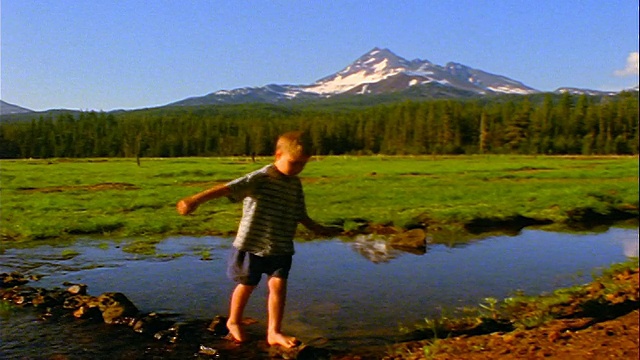 男孩走在溪流中的岩石在火花草甸/喀斯喀特山脉的背景/俄勒冈视频下载