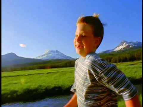 慢动作跟踪拍摄男孩在斯帕克斯草地/喀斯喀特山脉的背景/俄勒冈溪边奔跑视频下载