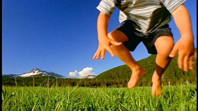 慢镜头男孩跳跃在草地上，朝摄像机/斯帕克斯草地，喀斯喀特山脉，俄勒冈州视频下载