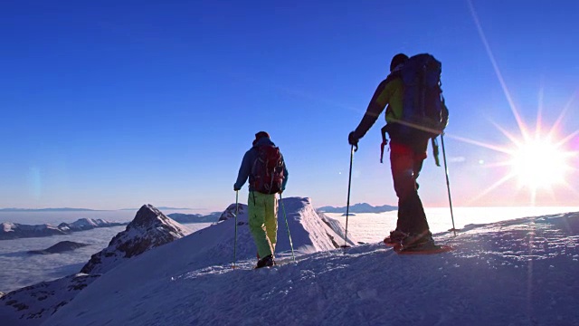 阳光普照的山顶上，穿着雪鞋的两名男子视频素材