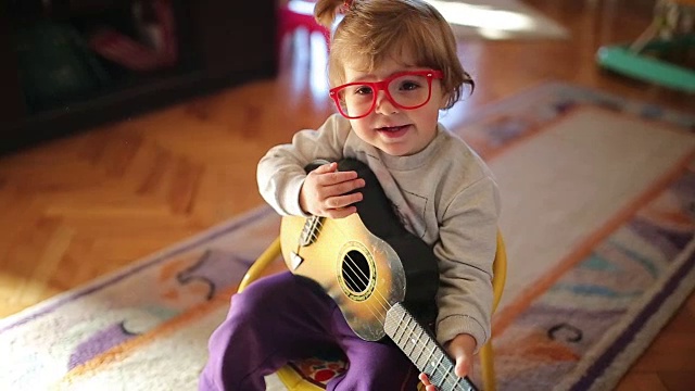 可爱的小女孩一边弹玩具吉他一边唱歌视频下载