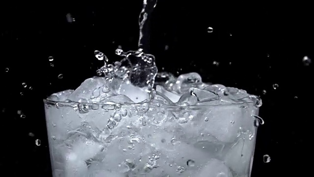 在黑色背景上以慢动作将水倒入冰杯视频素材