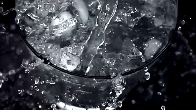 在黑色背景上以慢动作将水倒入冰杯视频素材