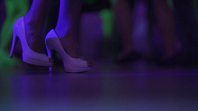 在夜总会或迪斯科舞厅的舞池上跳舞的女人和男人的脚的特写。围观穿着高跟鞋的美腿女人跳舞。视频素材