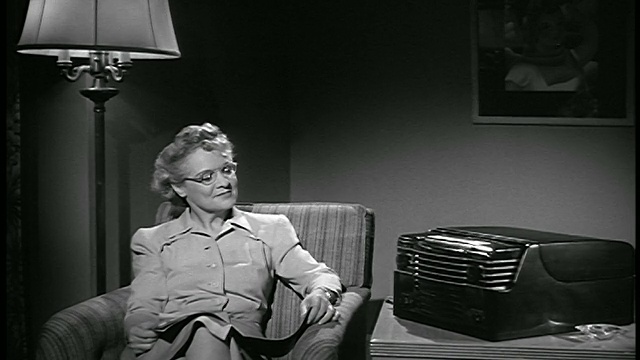 1947年老妇坐在扶手椅上阅读/检查手表+打开收音机/工业视频素材