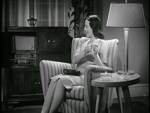 1947年，微笑的妇女坐在扶手椅上缝纫，听着收音机/工业视频素材