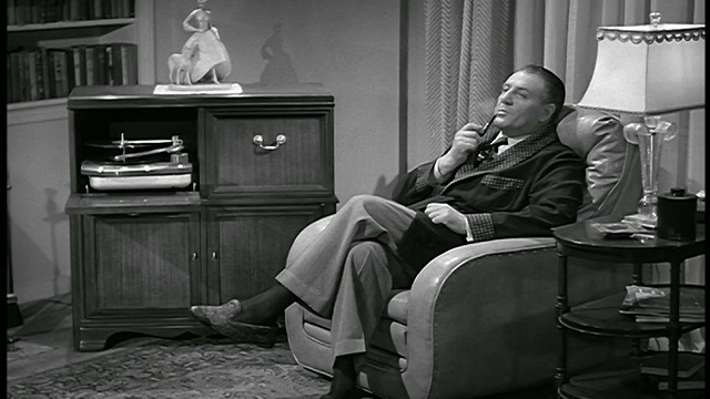 1950年B/W摄影车拍摄的男子坐在扶手椅上抽烟斗，听着唱机/工业视频下载