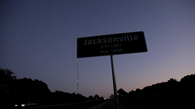 高速公路标志——“杰克逊维尔市极限流行”。13686，在暮色中汽车前灯从路上经过。视频素材
