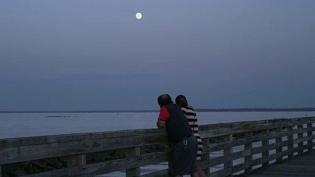 一对夫妇站在码头上观看超级月亮从长岛湾升起视频下载
