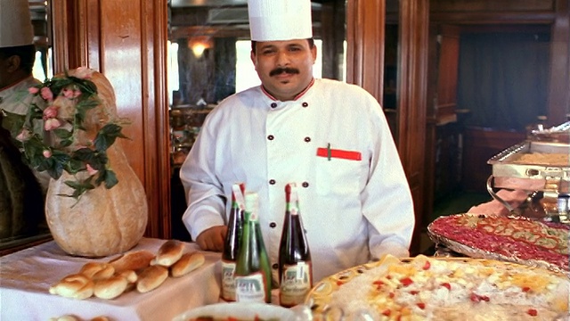 摄影车拍摄肖像胖乎乎的埃及厨师穿着制服站在桌子后面堆着食物微笑/埃及视频素材