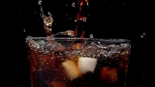 以慢动作将可乐苏打倒入装有冰块的黑色背景中视频素材
