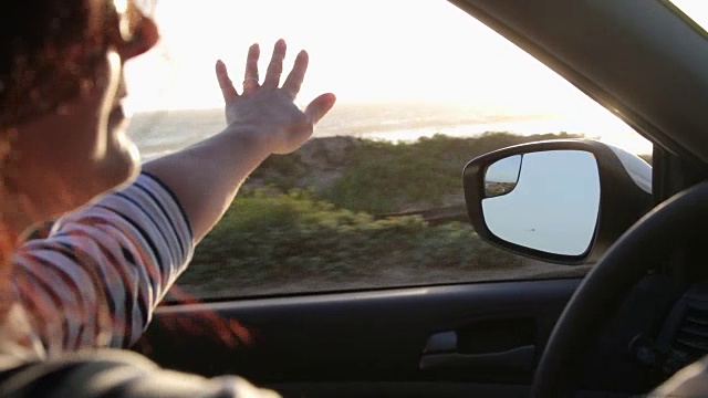 一个女人开着车，她把手伸出窗外去感受微风。视频素材