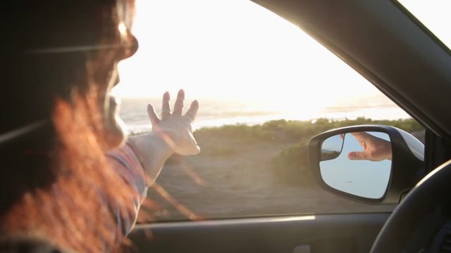 一个女人开着车，她把手伸出窗外去感受微风。视频素材