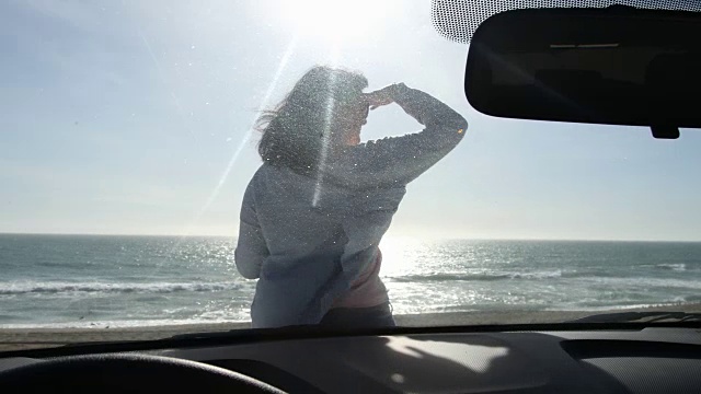 女人端着咖啡走到车前，望着大海。视频素材