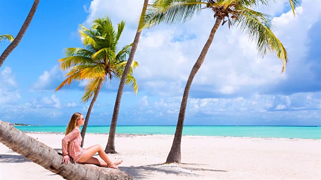 潘女士右，年轻女子坐在热带海滩的棕榈树上视频素材
