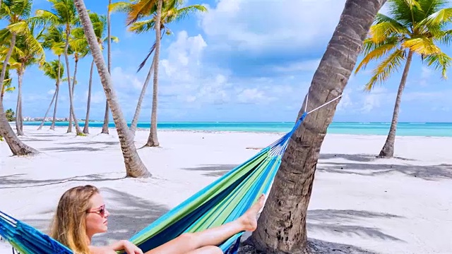 WS跟踪进来，一个年轻女子躺在热带海滩的吊床上视频素材