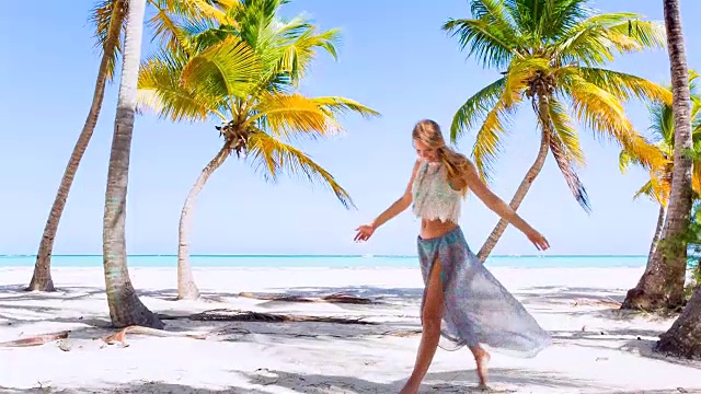 年轻女子在热带海滩的棕榈树下跳舞视频下载