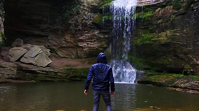 一个徒步旅行者凝视瀑布马尾在一个令人惊叹的风景与下雨的天气在一个公路旅行历险山脉的慢动作的观点。视频素材
