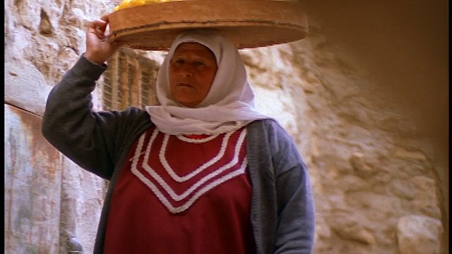 特写中年穆斯林妇女头上顶着一篮子食物走向摄像机/耶路撒冷视频下载