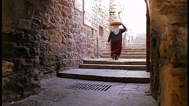 慢镜头后景耶路撒冷小巷里，一名穆斯林妇女头顶着篮子走上楼梯视频下载