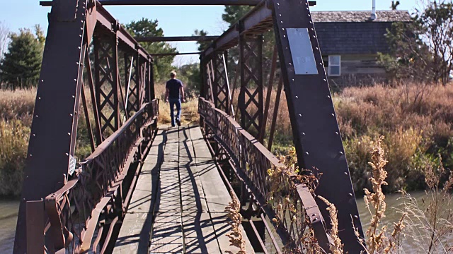 在美国农村，一个人走在横跨小溪的小铁桥上。视频素材