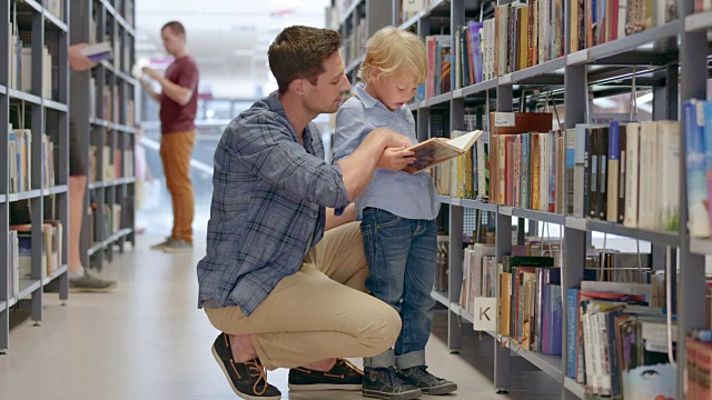 DS男孩和他的爸爸在图书馆的过道里看书视频素材
